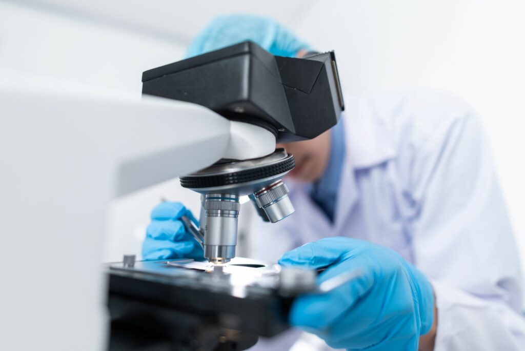Pracownik laboratorium pochylający się nad mikroskopem i obserwujący materiał badawczy.